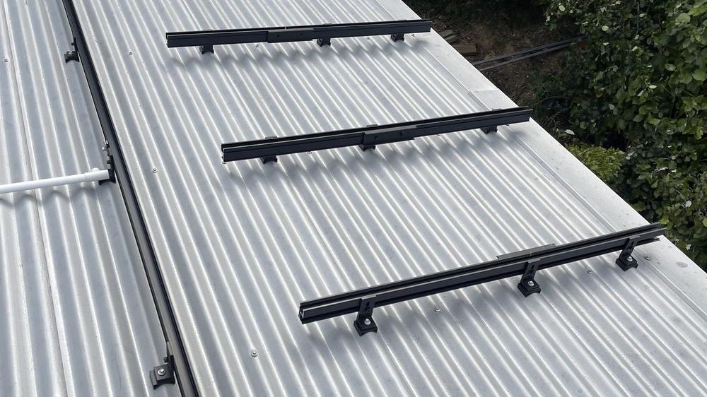 Black mounting rails fixed across a corrugated steel roof
