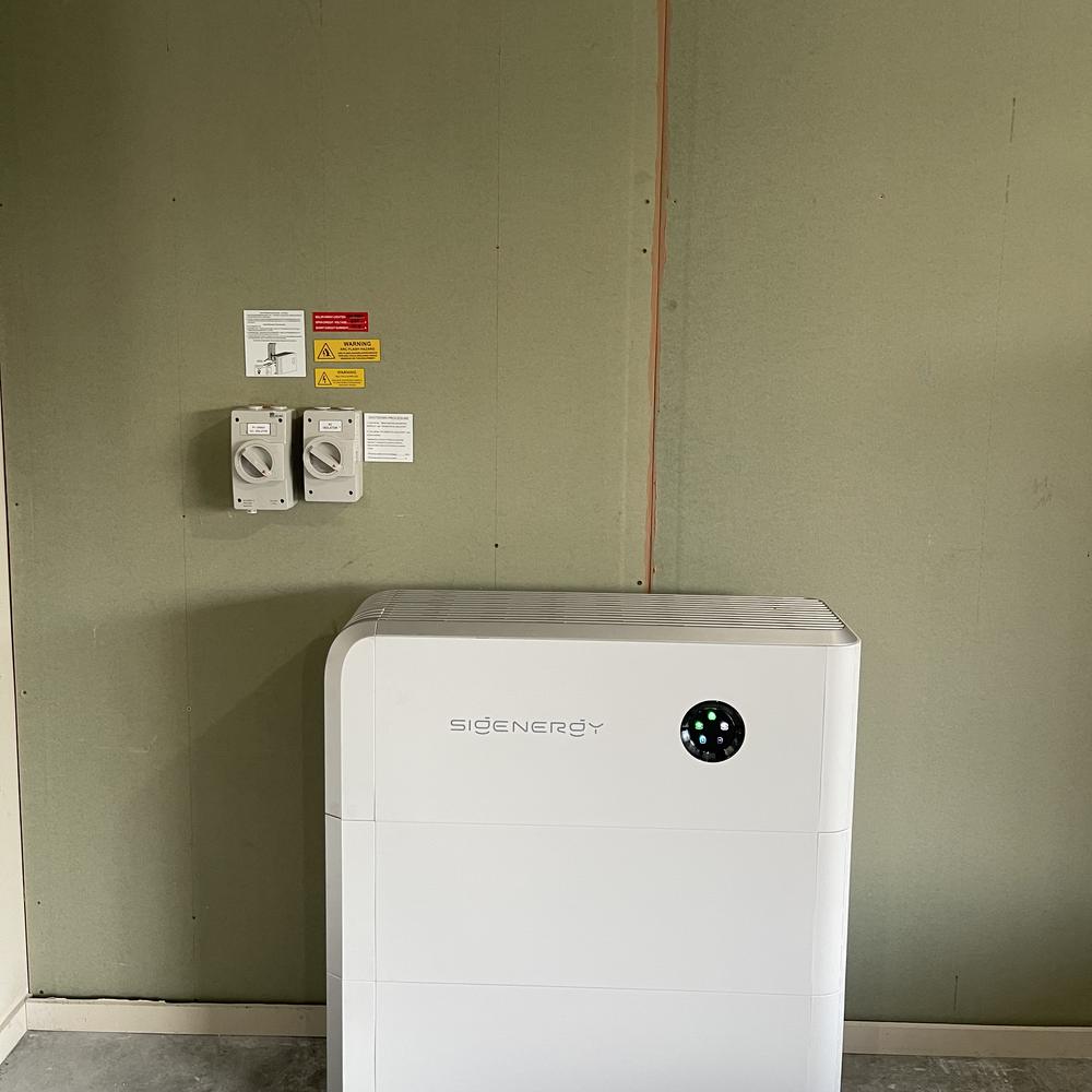 Floor-standing Sigenergy home battery with isolator switches on the wall above it