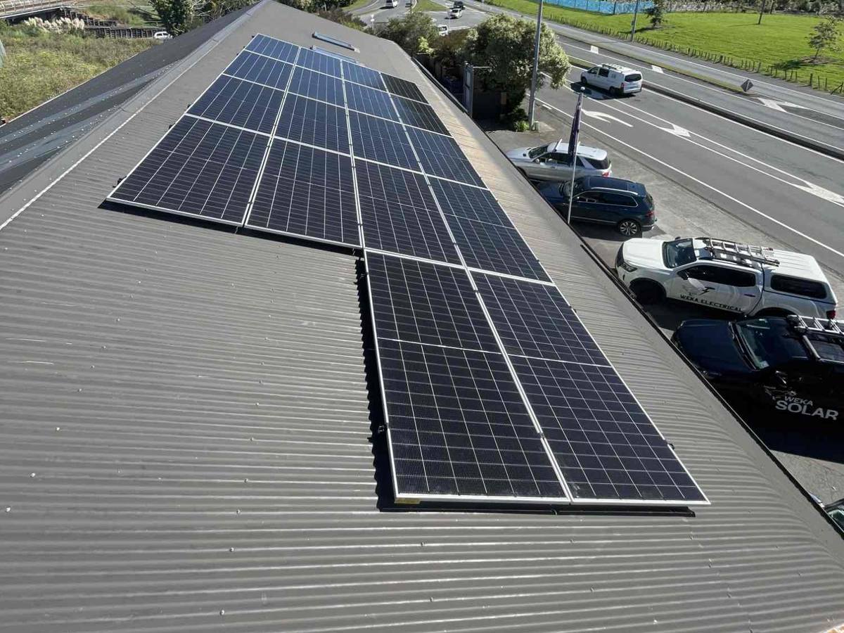 A commercial solar array on a long-run metal roof beside the highway, with bush-covered hills behind