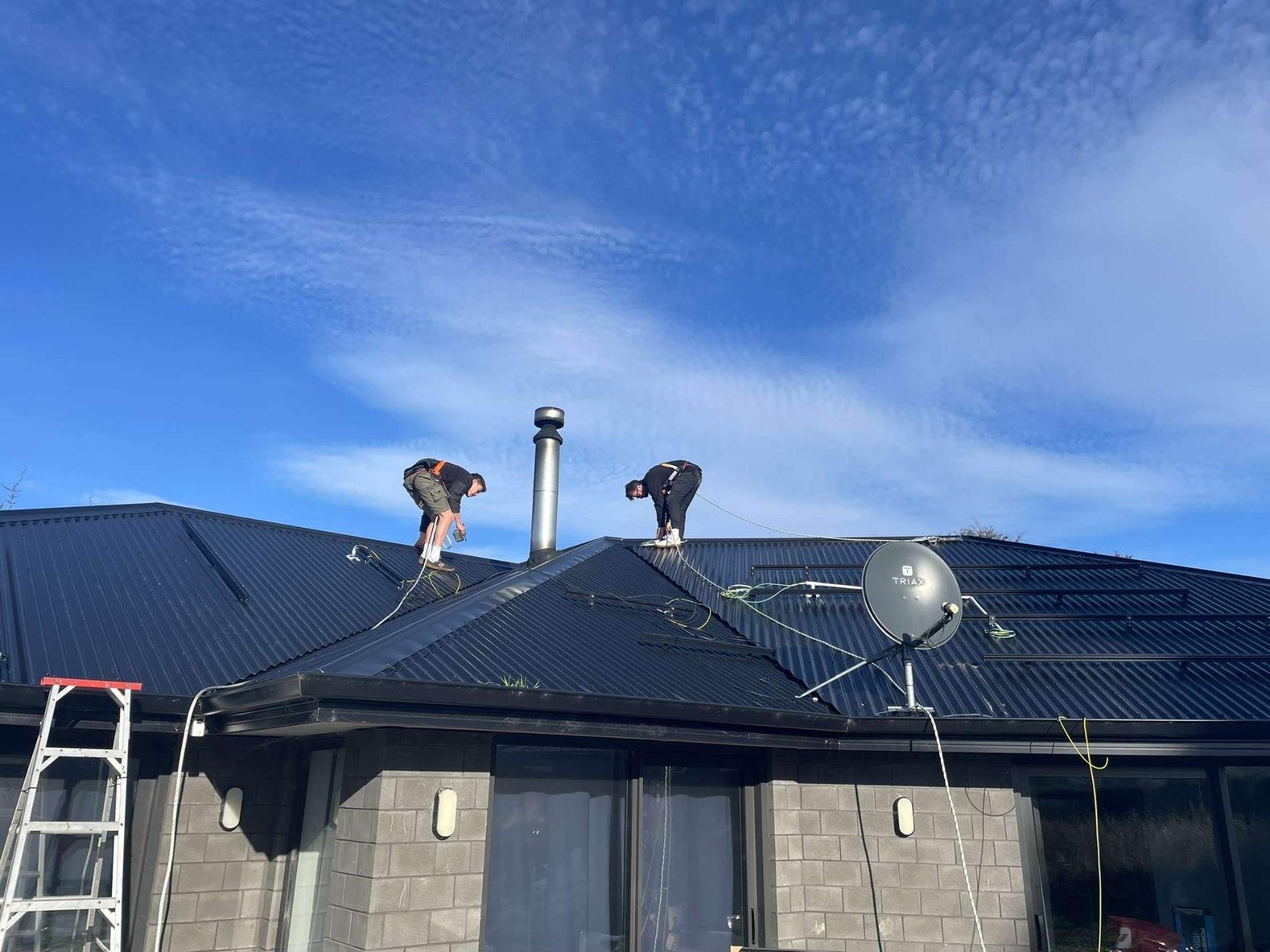 Two Weka Solar installers working on a dark metal roof