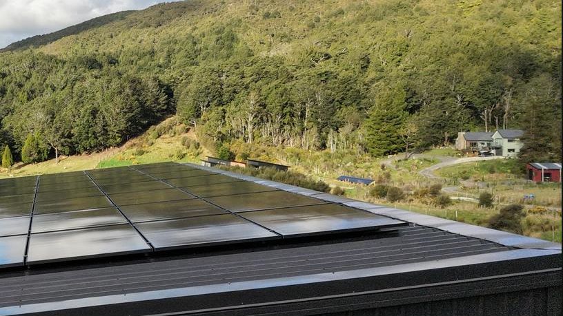 A 34-panel solar array on a low-pitch roof in Whitemans Valley, bush hills behind