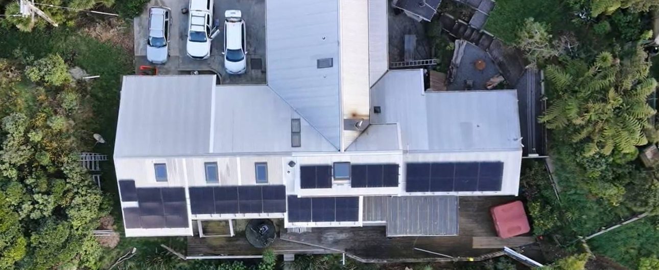 Aerial view of a 35-panel solar system across the roof planes of a Paekākāriki home ringed by native bush